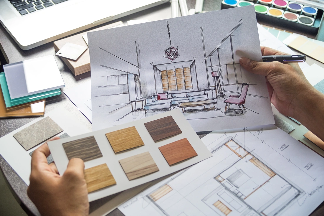 Hands holding an interior design sketch above floor plans and material samples
