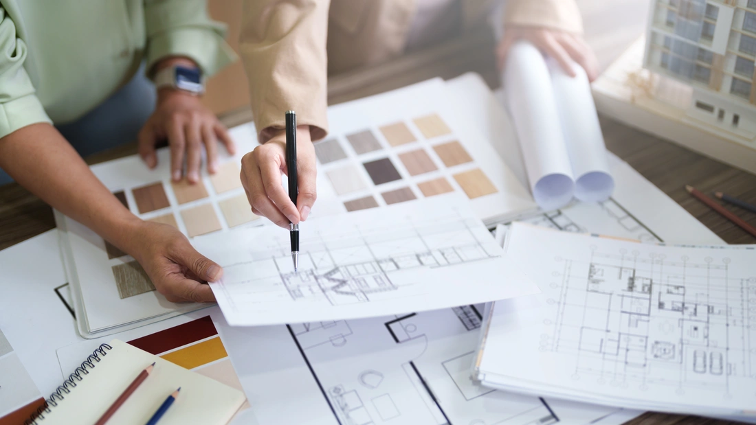 Two people reviewing floor plans alongside finish samples and rolled drawings